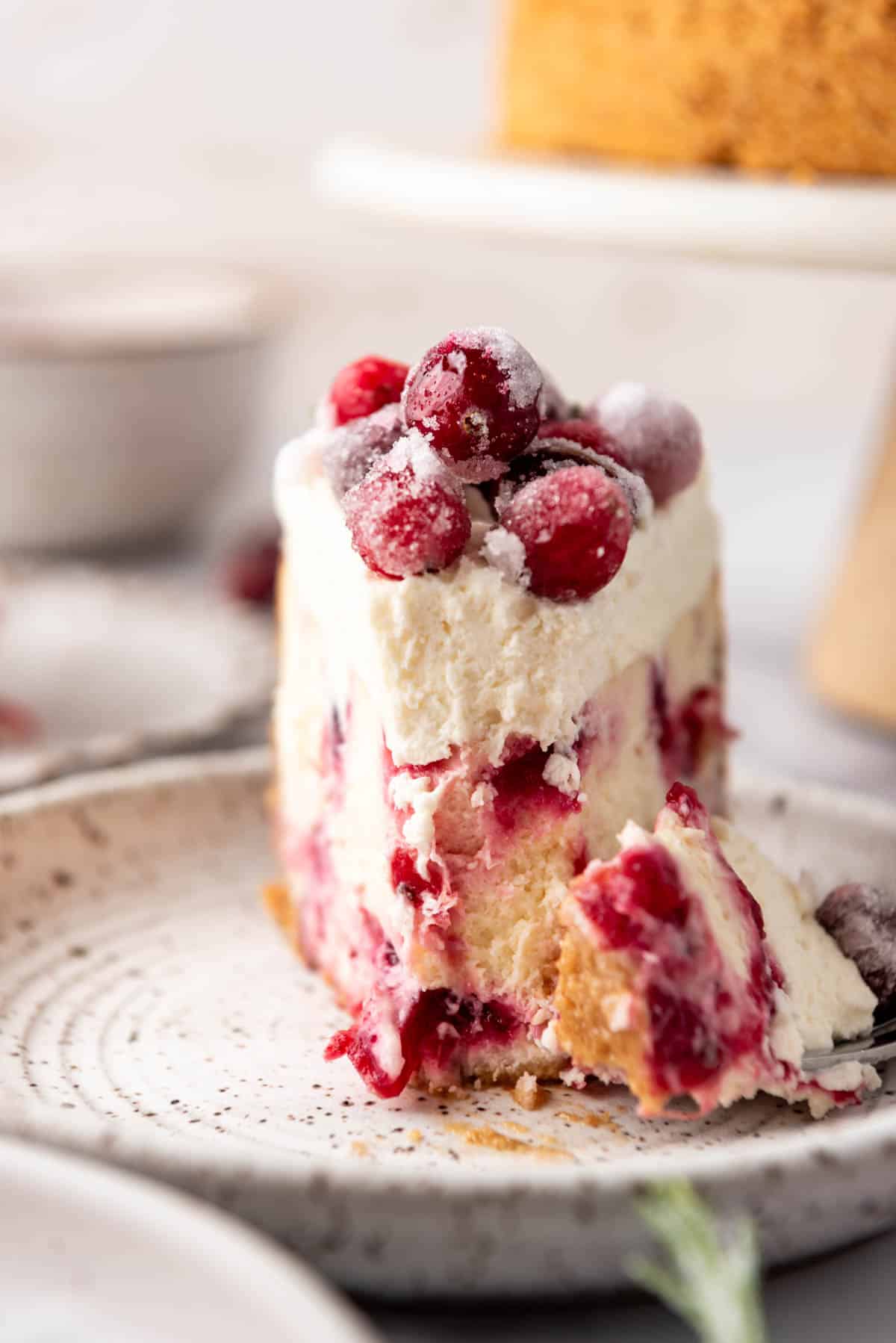 A close up image of a piece of cranberry cheesecake with a bite taken out of it on a plate.