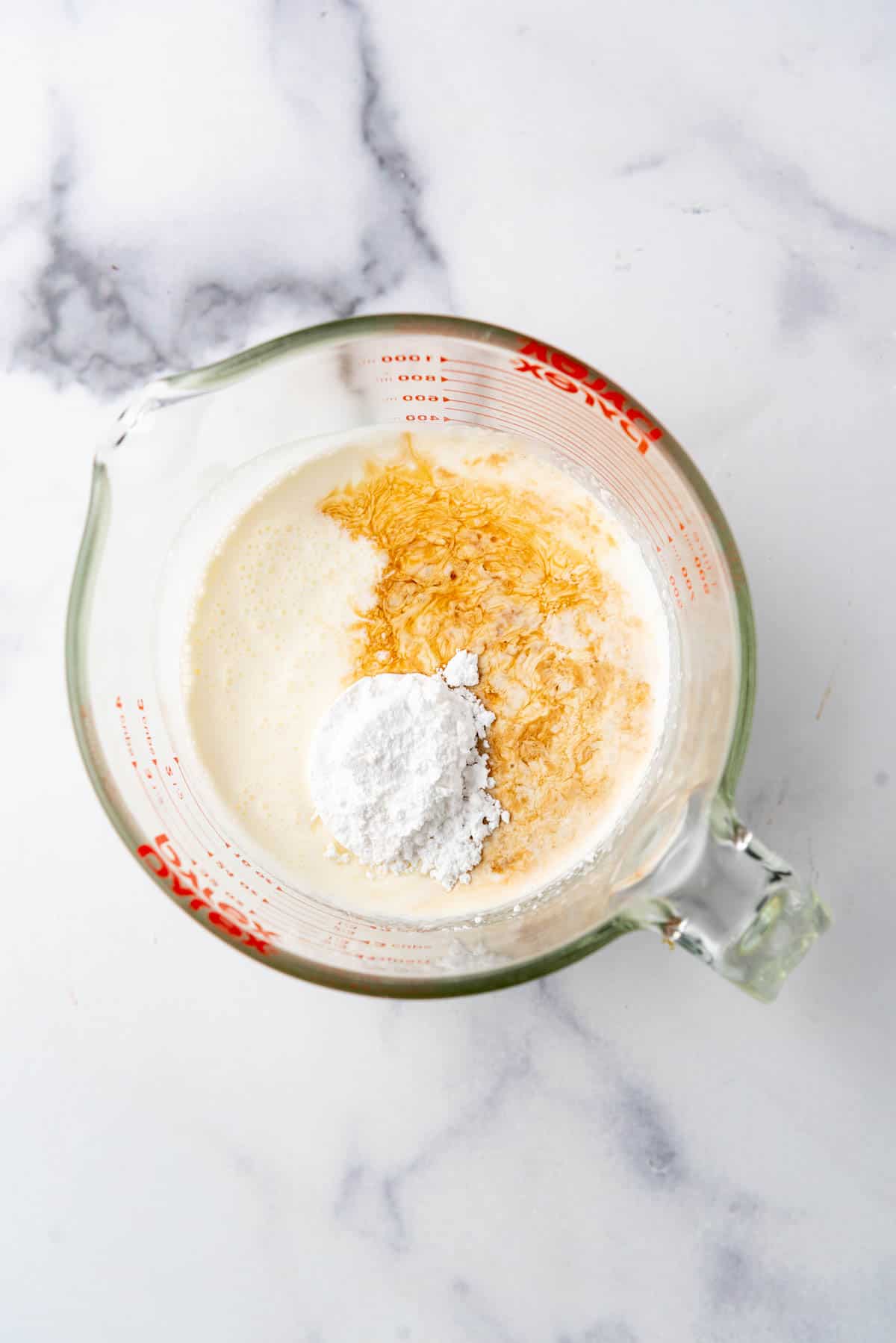 Heavy cream, vanilla extract, and powdered sugar in a glass bowl.