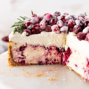 A side angle view of a cranberry cheesecake with a few slices removed.