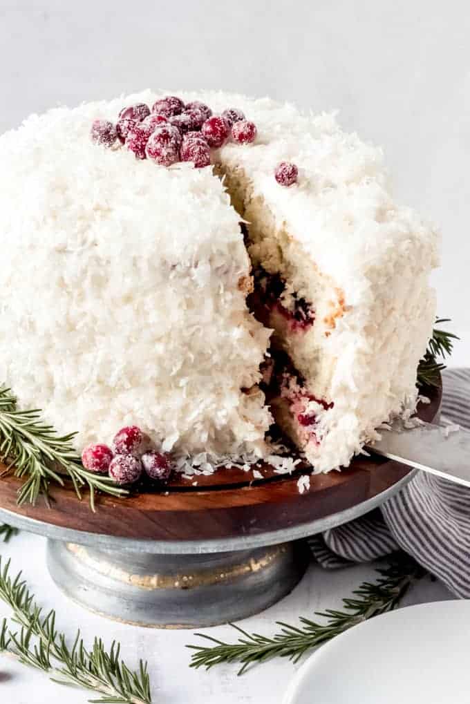 An image of a cranberry coconut cake decorated with sugared cranberries and sprigs of rosemary.