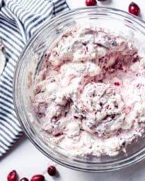 An image of a bowl of fluffy pink dessert salad made with fresh cranberries, pineapple, marshmallows, and whipped cream.