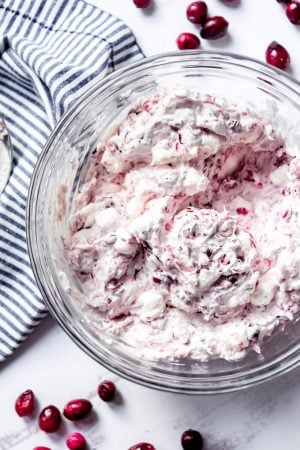 An image of a bowl of fluffy pink dessert salad made with fresh cranberries, pineapple, marshmallows, and whipped cream.