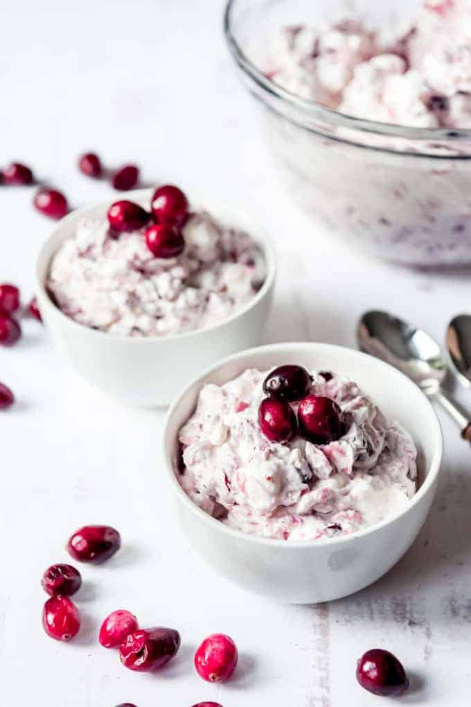 An image of two white bowls filled with cranberry fluff salad and garnished with fresh cranberries.