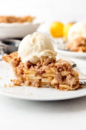 Dutch apple pie on a white plate with ice cream on top and more pie and ice cream in the background