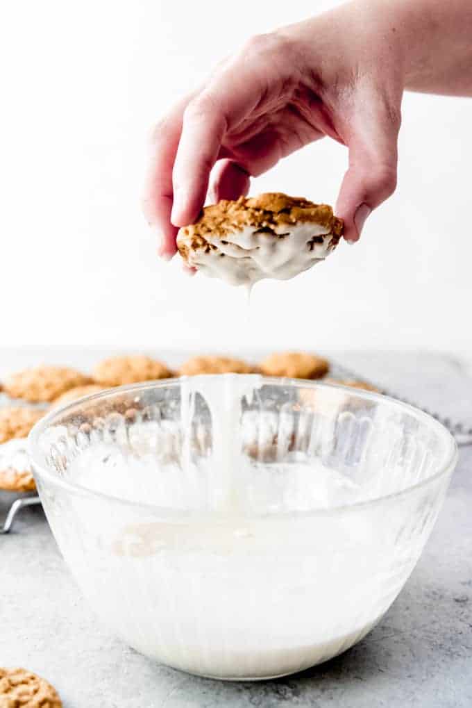 An image of an oatmeal cookie being dipped in a simple vanilla glaze.