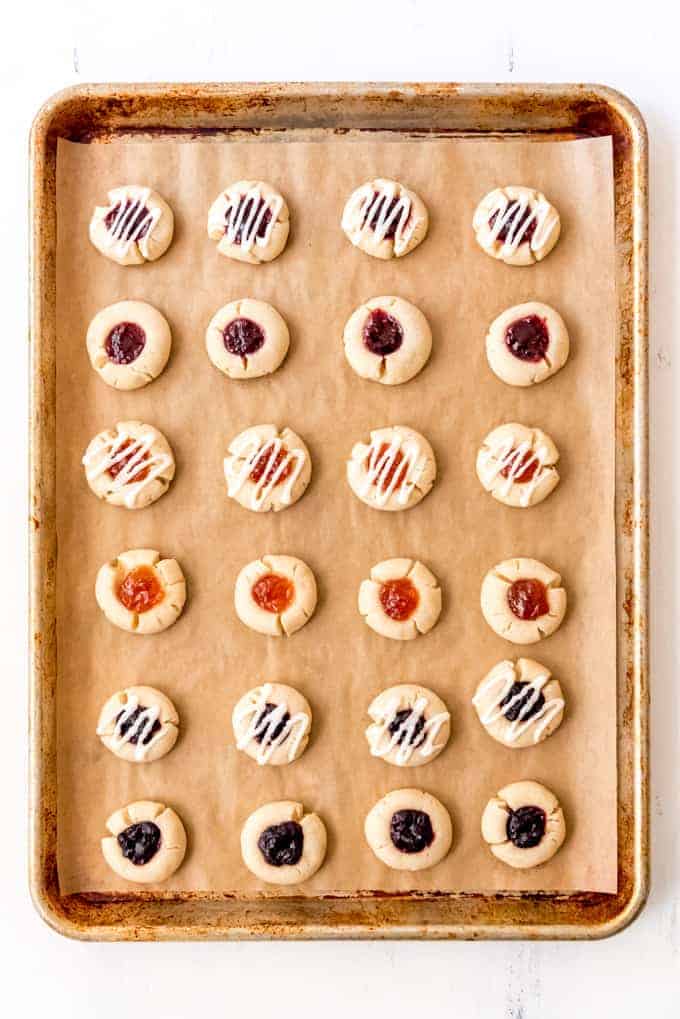 An image of a baking sheet with jam thumbprint cookies on it.