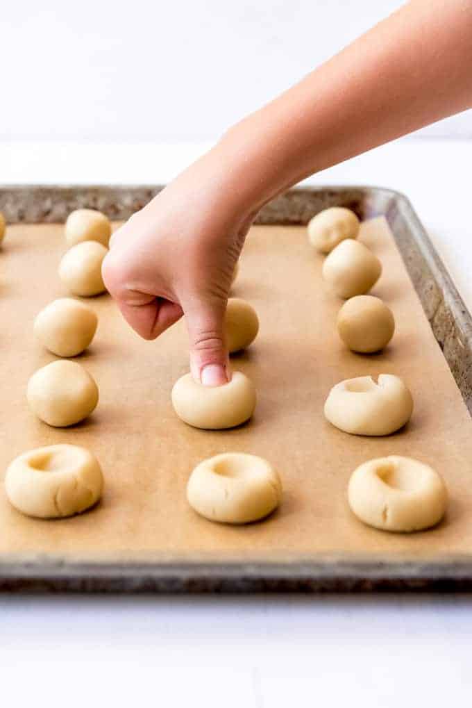 An image of a thumb pressing into balls of cookie dough to make an impression for jam filling.