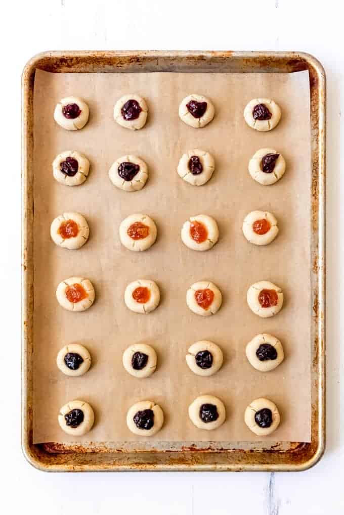 An image of jam thumbprint cookies on a baking sheet.