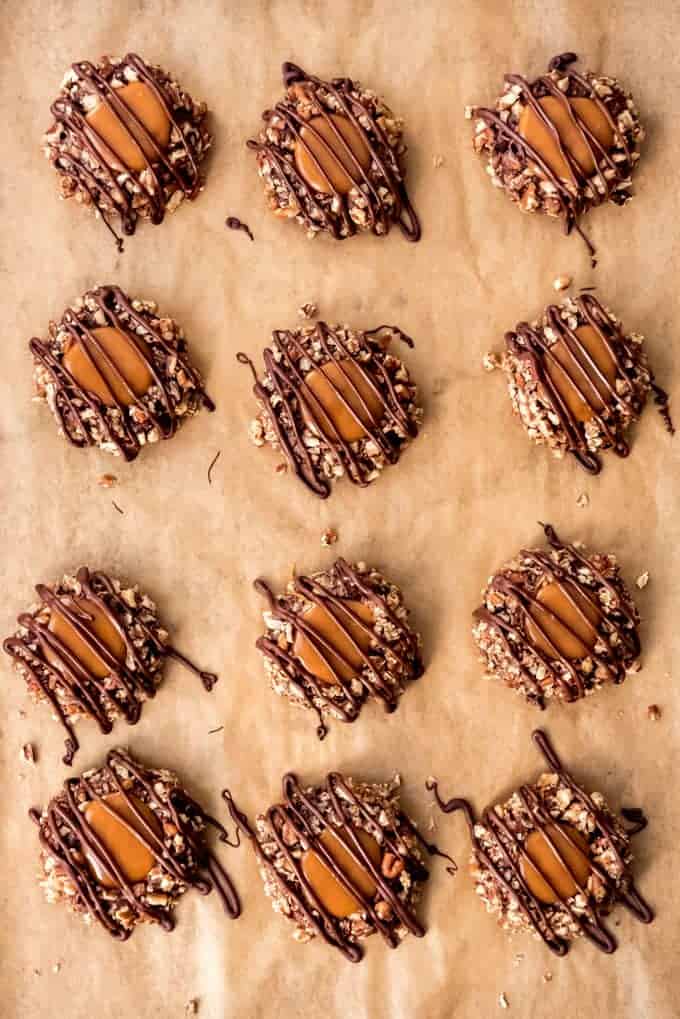 An image showing chocolate caramel thumbprint turtle cookies with melted chocolate drizzled over the top on a baking sheet.
