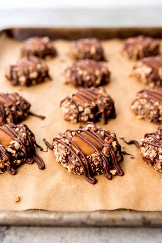 An image of turtle thumbprint cookies with chocolate drizzled over the top.