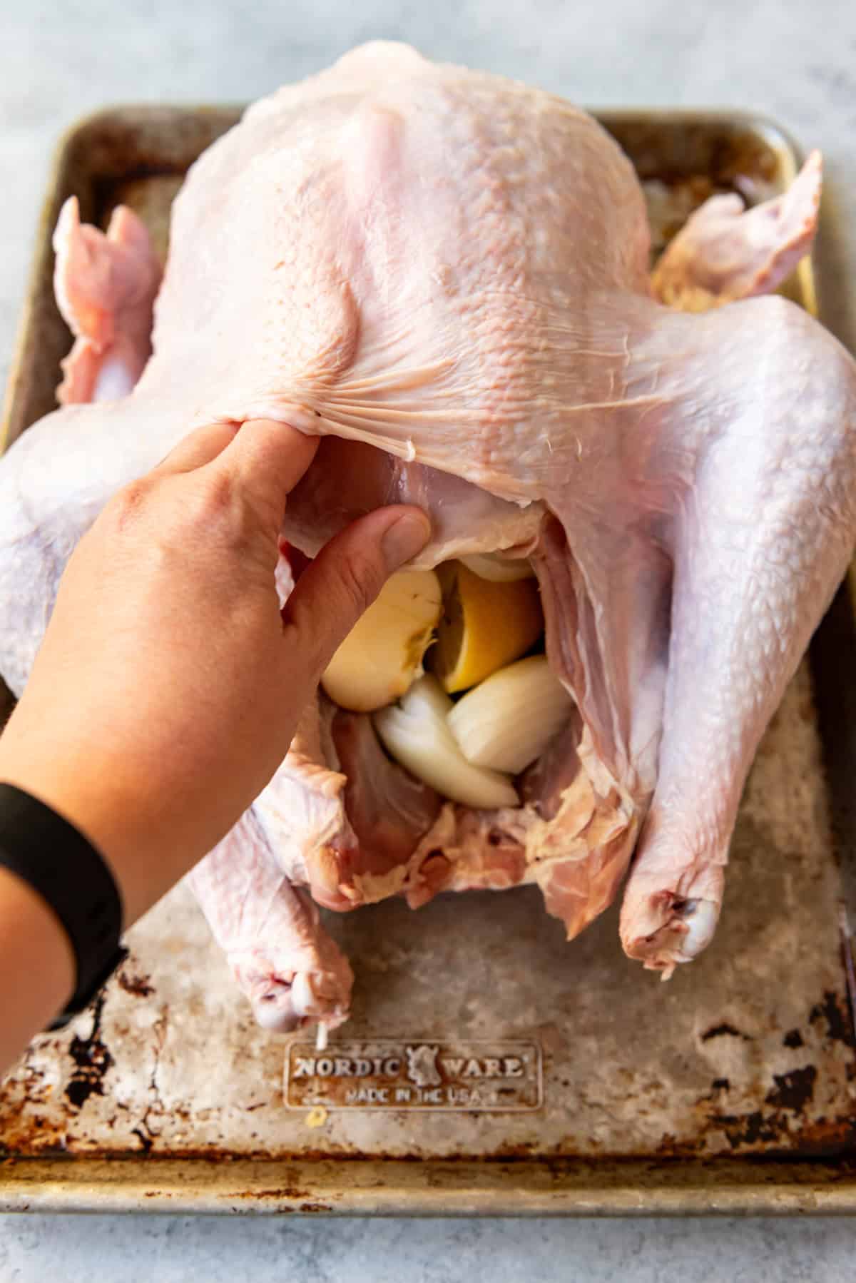 An image of a hand loosening the turkey skin from the turkey meat on a whole turkey.