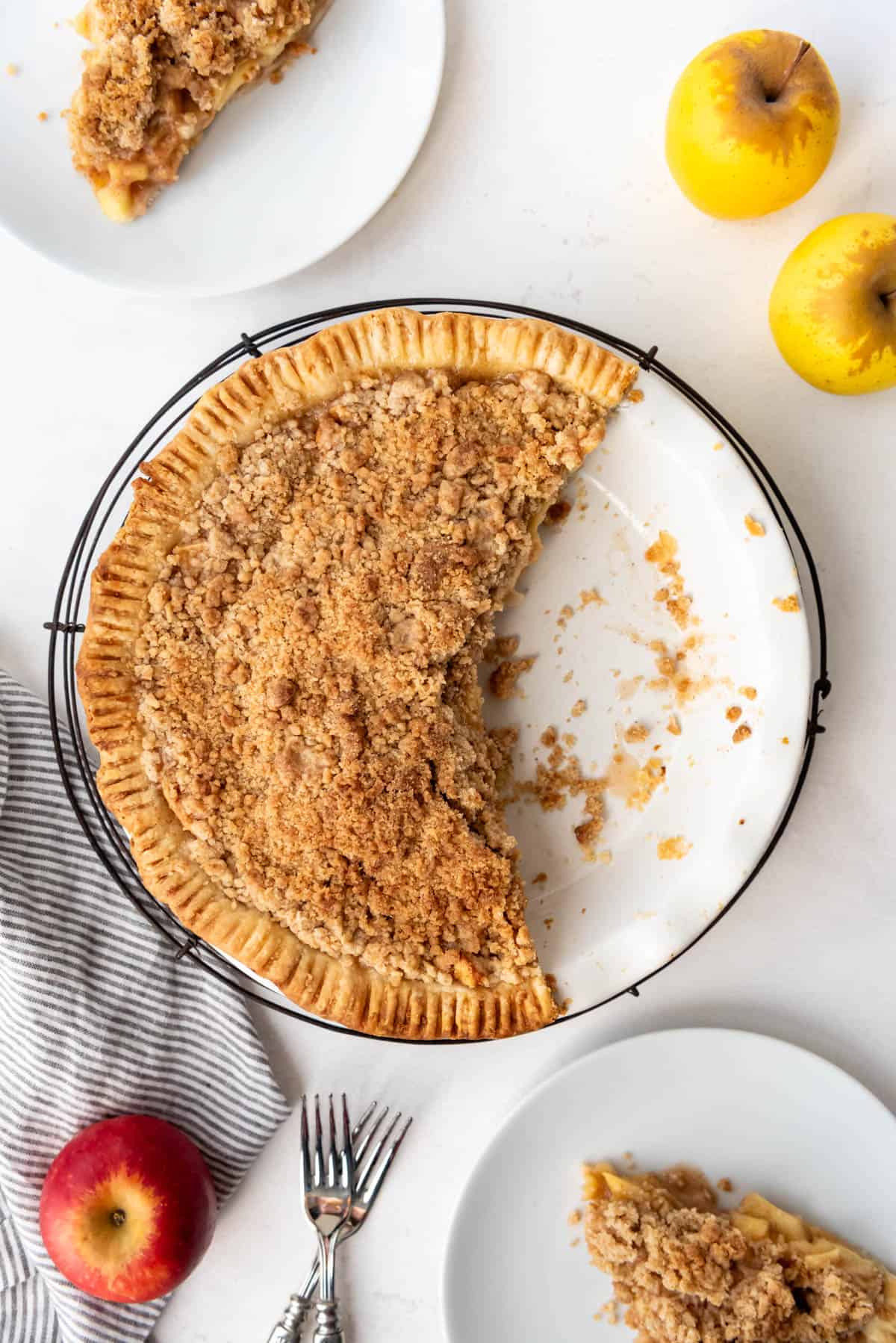 An image of an apple crumble pie with some slices removed and served on white plates.