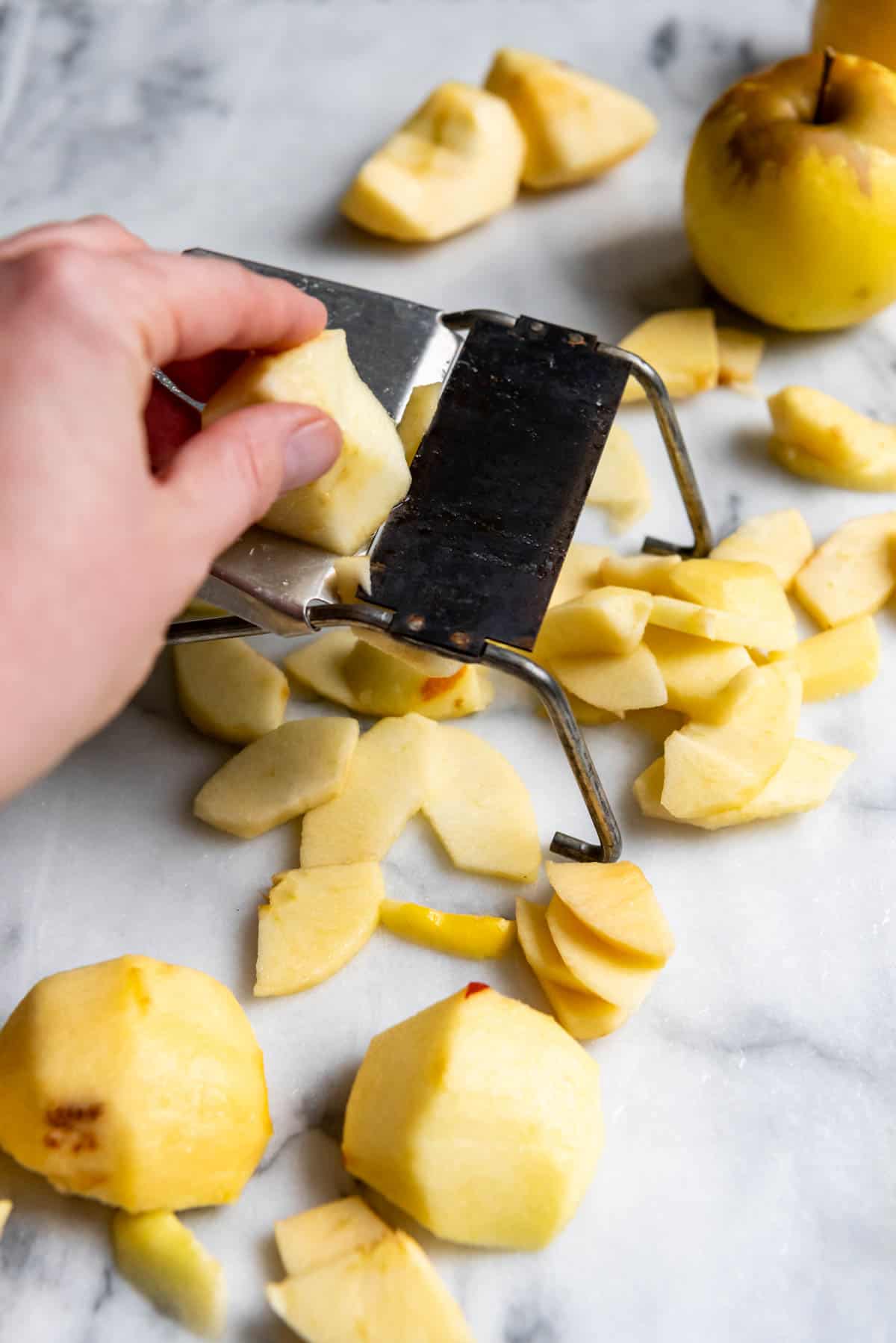 An image of apples being sliced 1/4" thick for apple pie using a mandoline slicer.