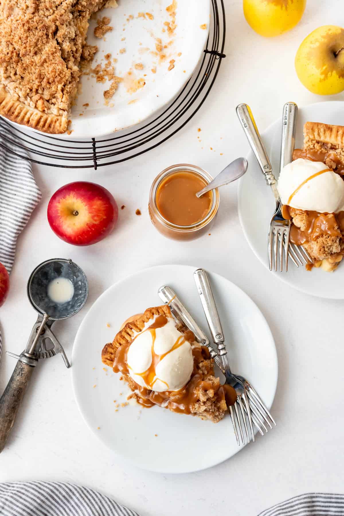 An image of piece of apple crumble pie with a scoop of ice cream and caramel sauce on a white plate.