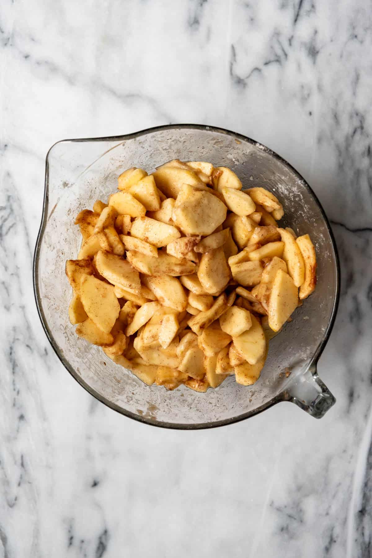 An image of a bowl full of sliced apples tossed with flour, sugar, and cinnamon for pie filling.