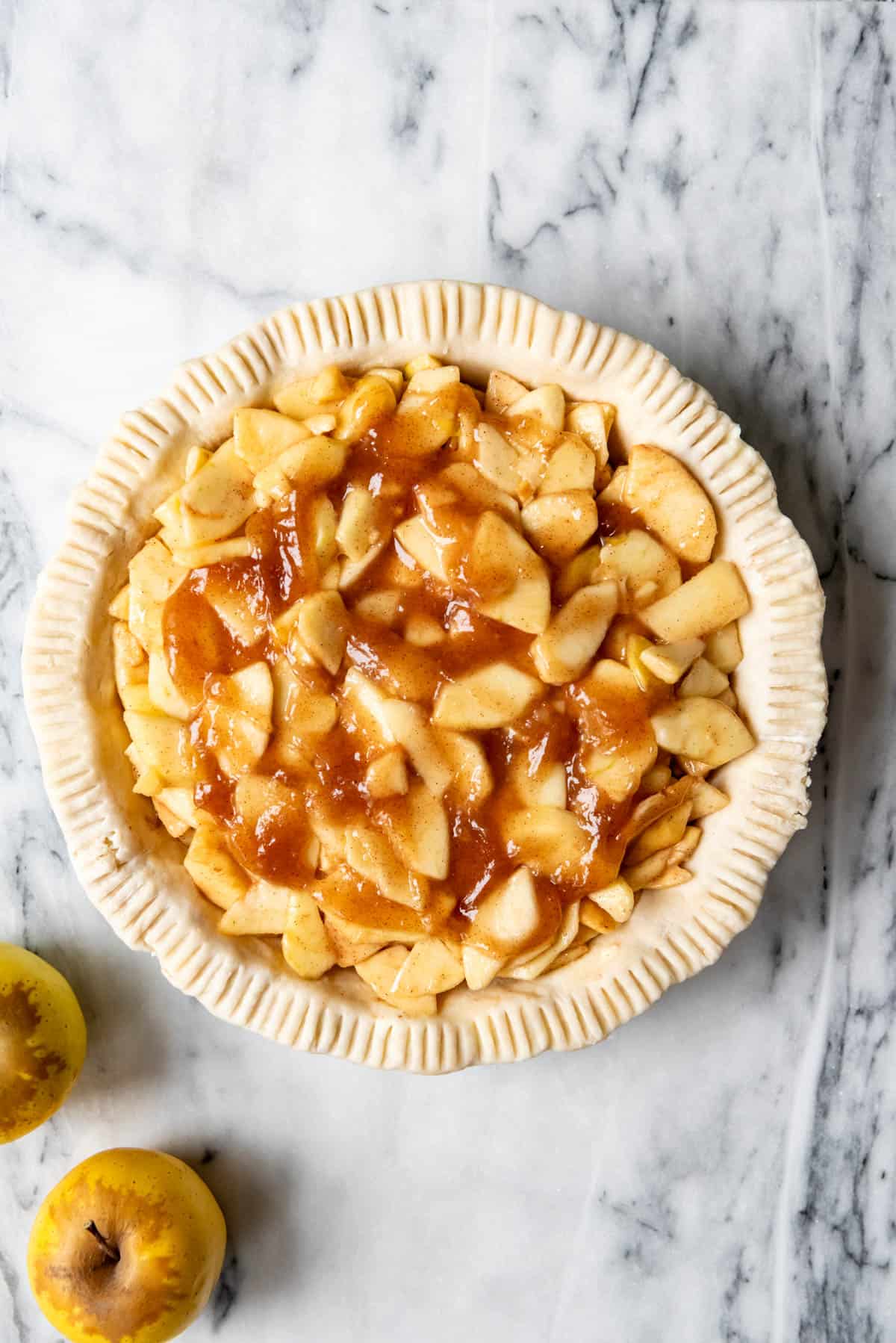 An image of an unbaked pie crust filled with apple pie filling.