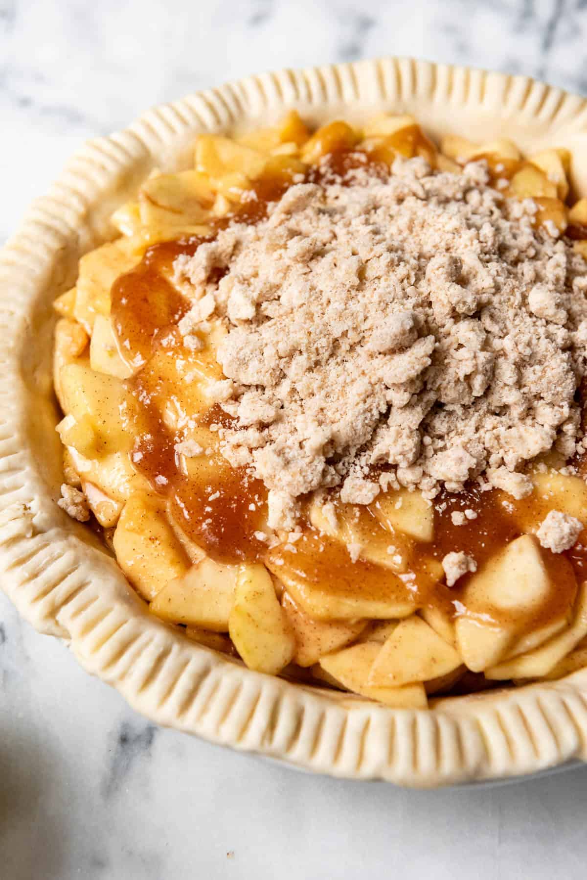 An image of an unbaked pie crust filled with apple pie filling and being topped with a crumb topping.