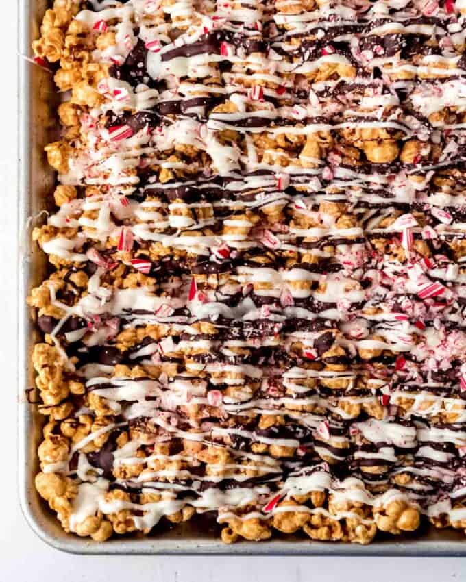 An image of homemade gourmet caramel popcorn on a baking sheet drizzled with white and dark chocolate and crushed candy canes.