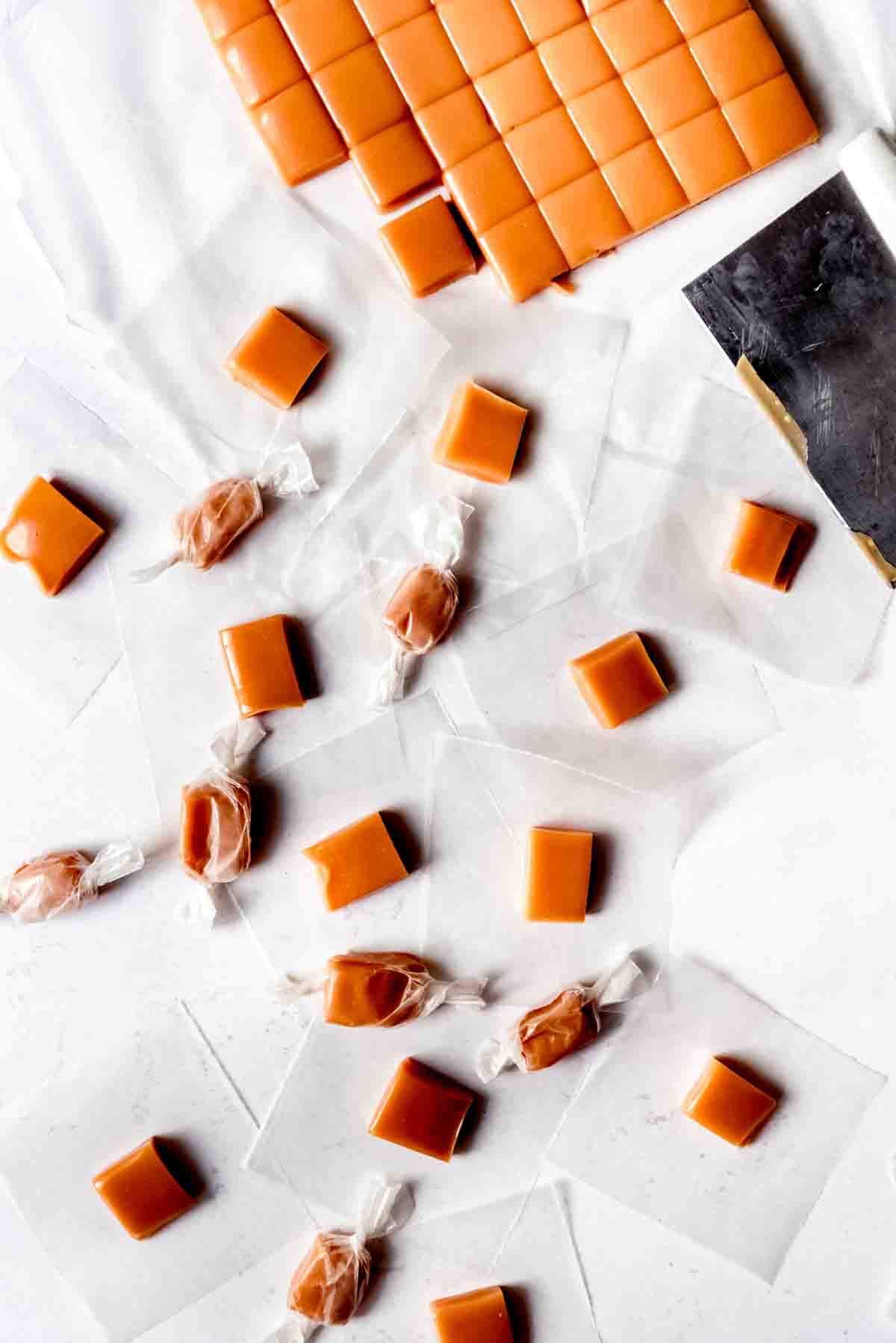 An image of homemade cream caramels in the process of being cut into squares and wrapped in wax paper.