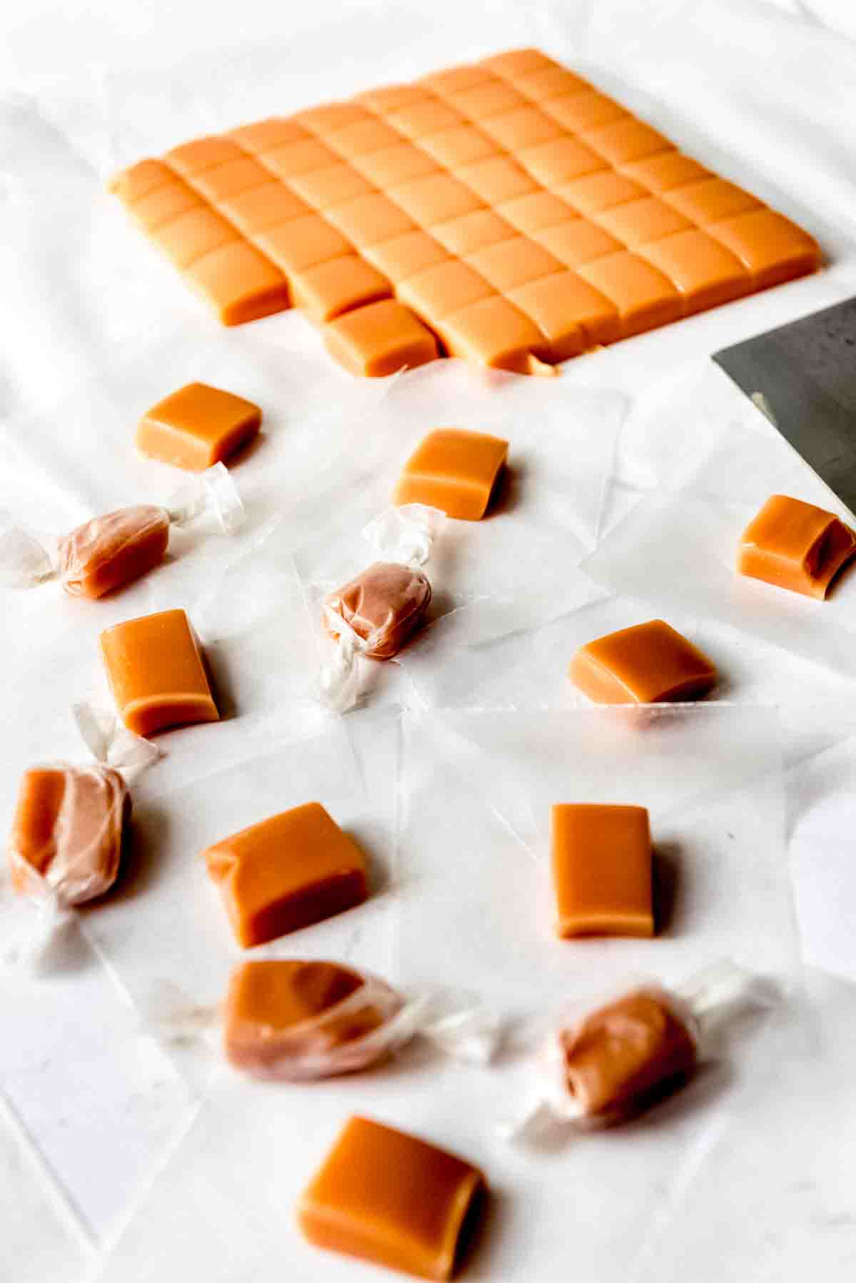 An image of homemade caramels being cut and wrapped in waxed paper.