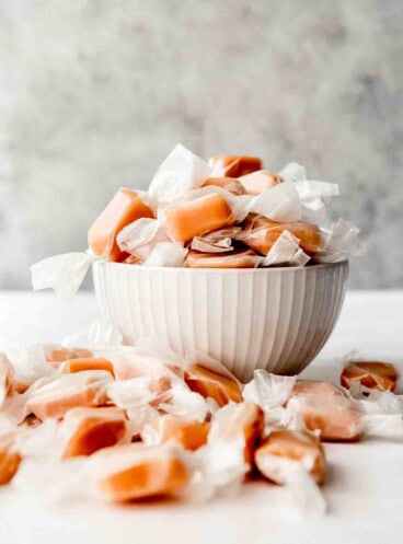 An image of homemade caramels wrapped in wax paper in a bowl.