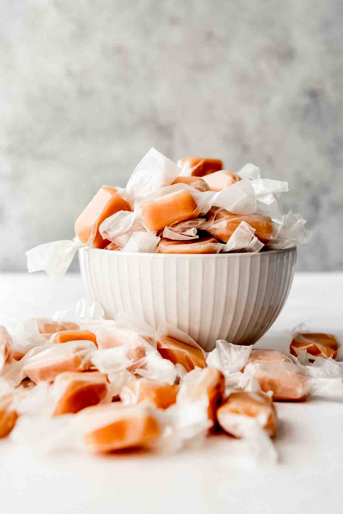 An image of homemade caramels wrapped in wax paper in a bowl.