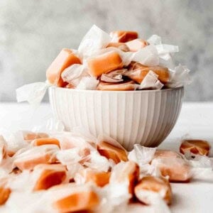 An image of homemade caramels wrapped in wax paper in a bowl.