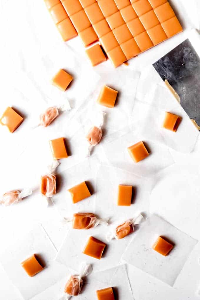An image of homemade cream caramels in the process of being cut into squares and wrapped in wax paper.