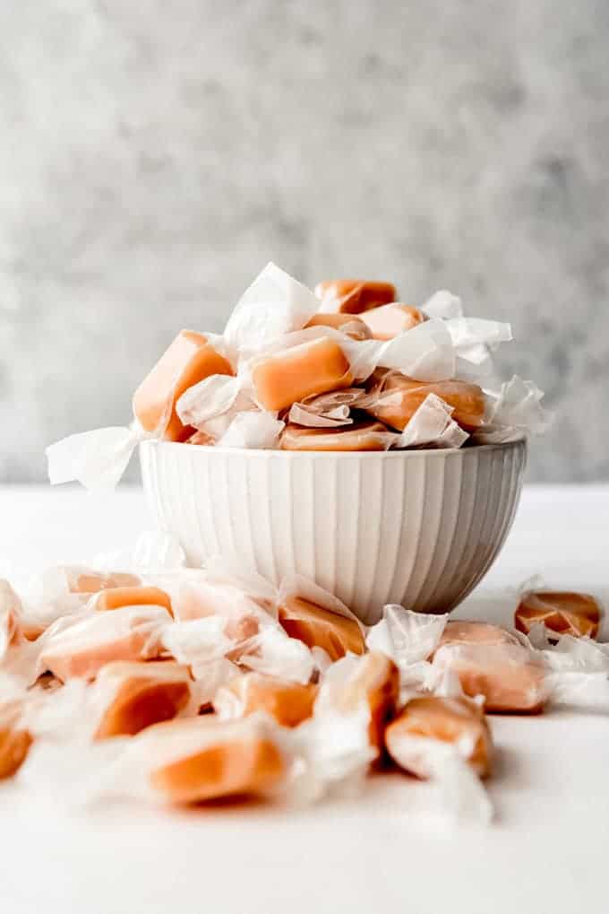 An image of homemade caramels wrapped in wax paper in a bowl.
