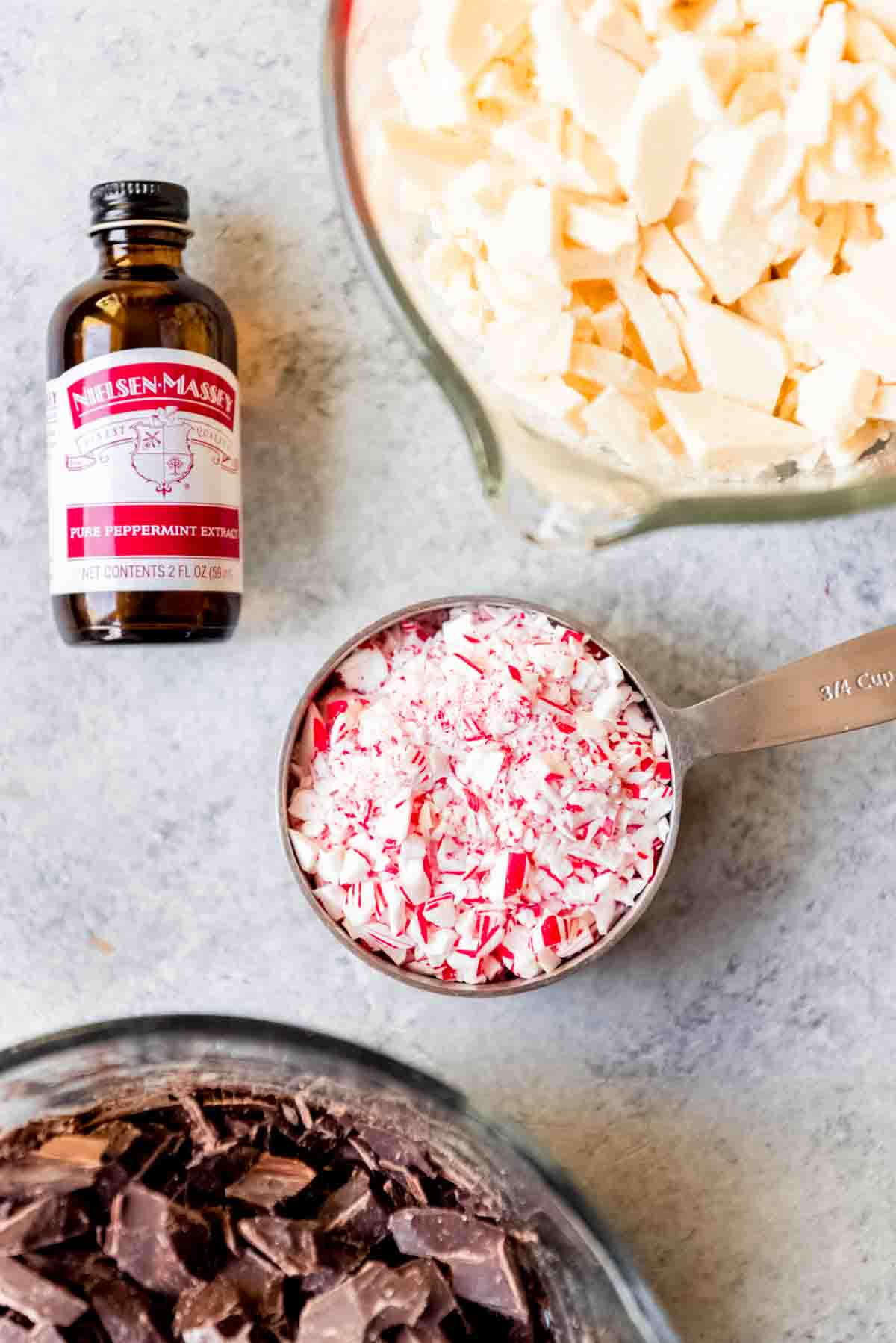 Crushed candy cane pieces in a measuring cup next to bowls of chopped dark chocolate and white chocolate.