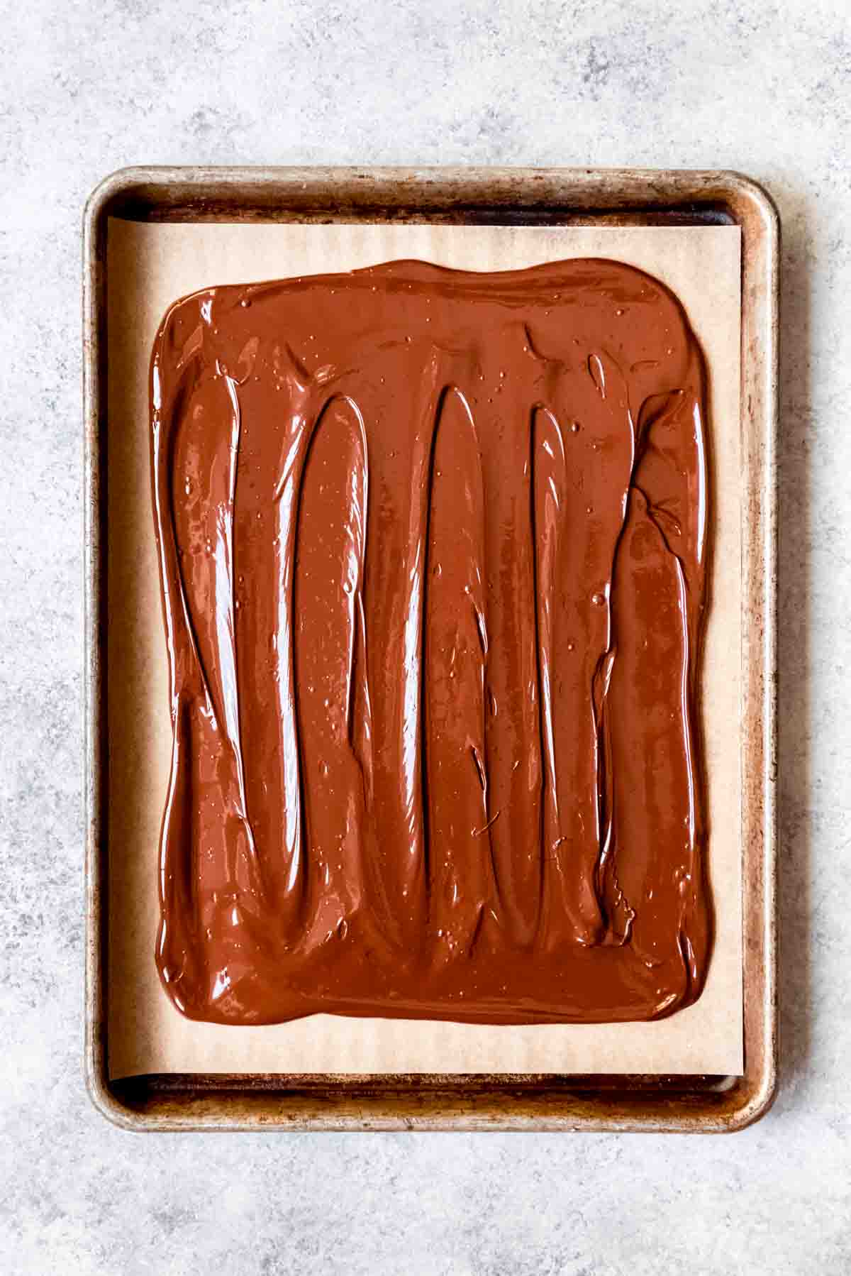 Melted dark chocolate spread onto parchment paper on a baking sheet.