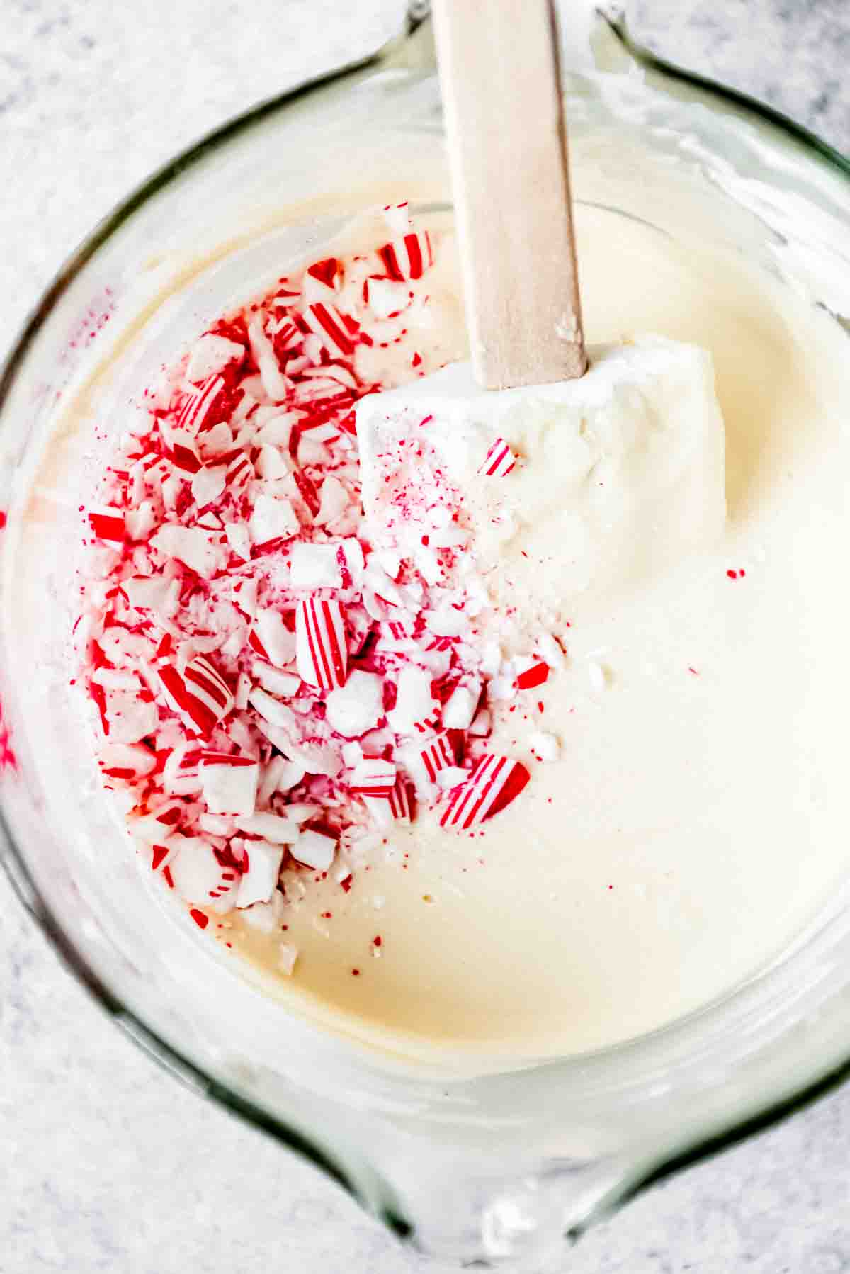 Adding crushed candy cane pieces to melted white chocolate in a bowl.