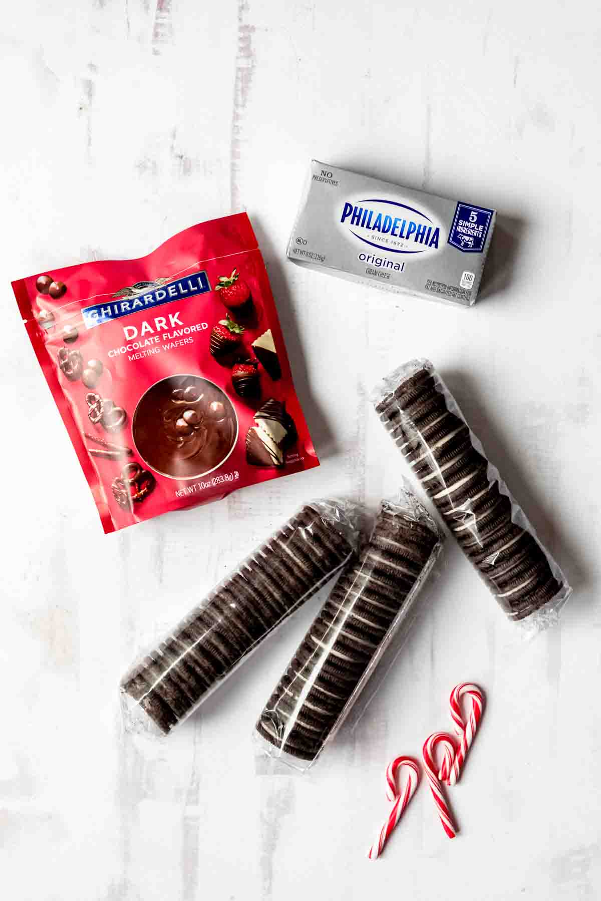 An image of dark melting chocolates, Oreo cookies, cream cheese, and candy canes on a white surface.