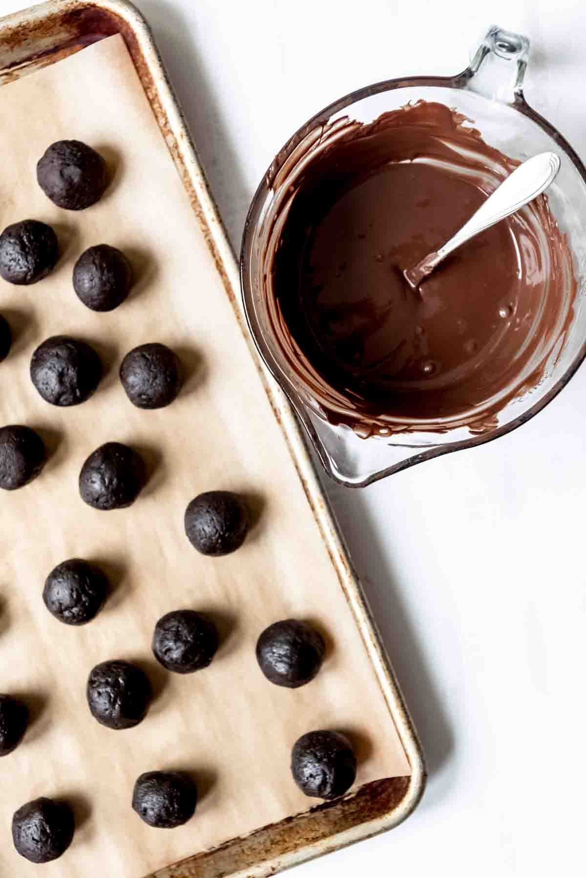 An image of balls of crushed Oreos mixed with cream cheese next to a bowl of melted dark chocolate for dipping.