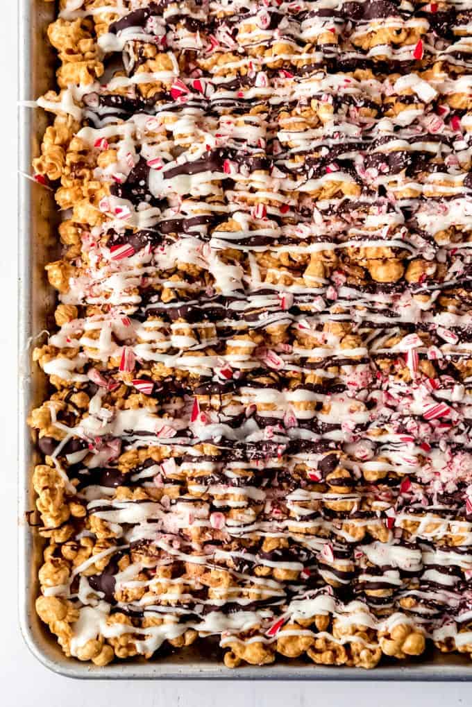 An image of homemade gourmet caramel popcorn on a baking sheet drizzled with white and dark chocolate and crushed candy canes.
