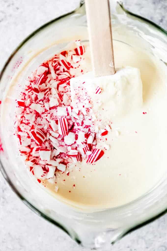 An image of crushed peppermint candy canes being stirred into melted white chocolate.