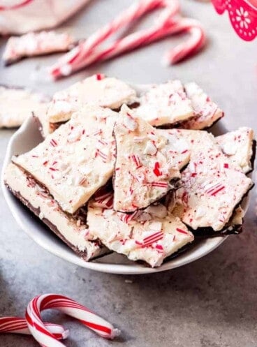 An image of pieces of homemade peppermint bark in a bowl next to some candy canes.