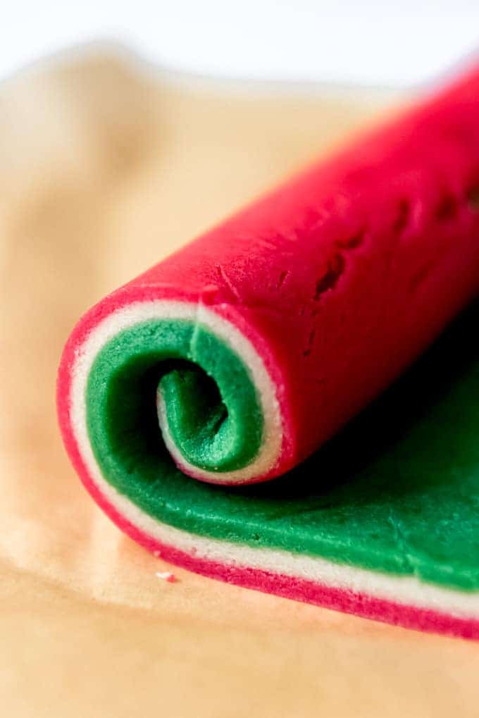 An image of three colored layers of sugar cookie dough being rolled up to create pinwheel cookies.