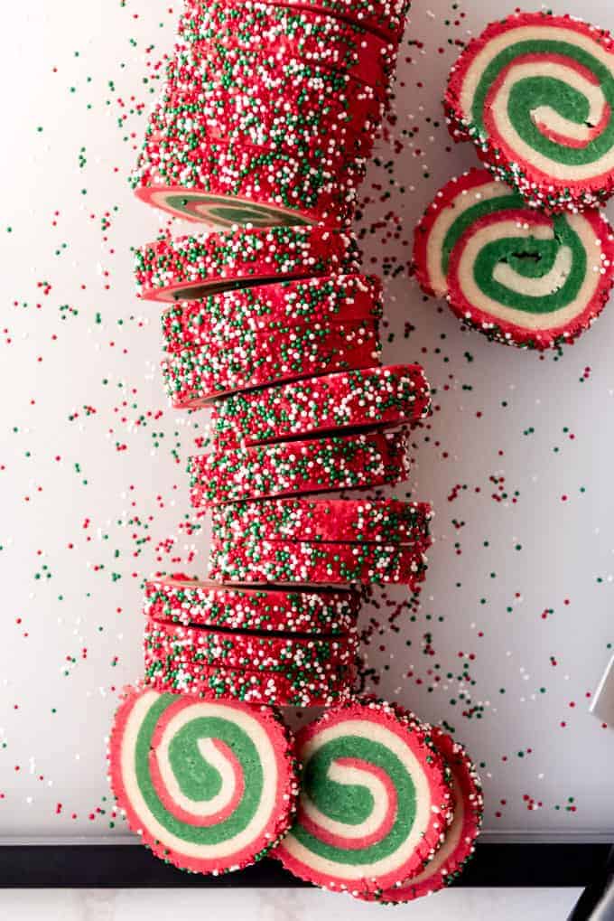 An image of a log of sugar cookie dough rolled in holiday nonpareils being sliced into individual cookies.