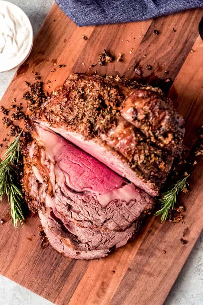 Sliced prime rib roast on wooden board with fresh rosemary