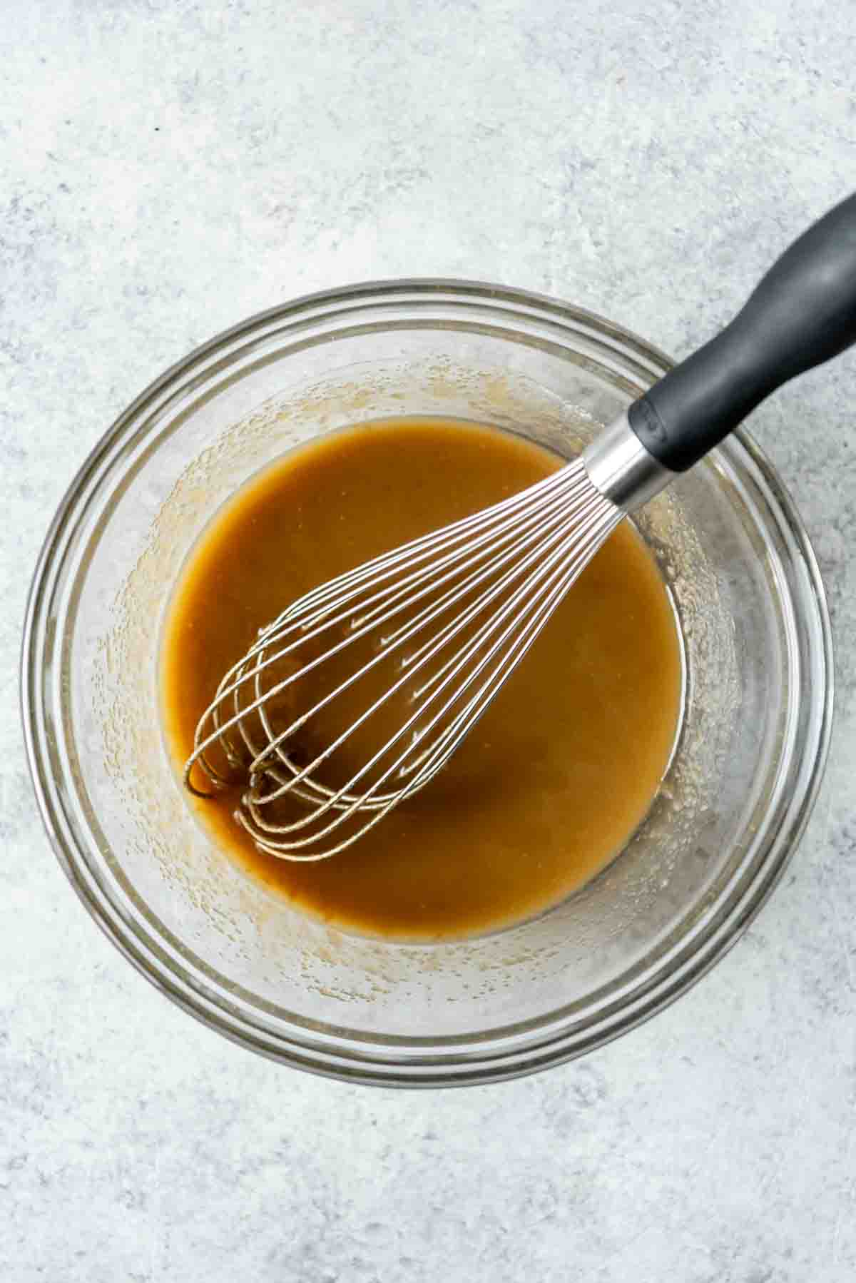 Whisked melted butter and sugar in a bowl with a whisk.