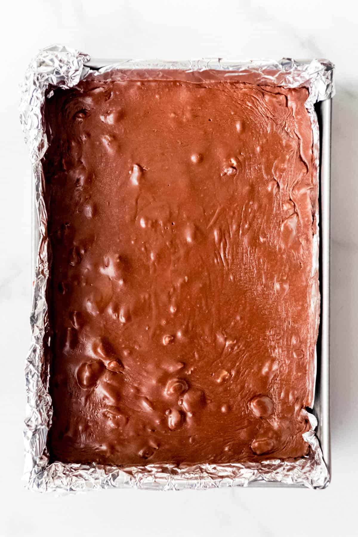 An image of chocolate walnut fudge in a 9x13-inch pan lined with aluminum foil.