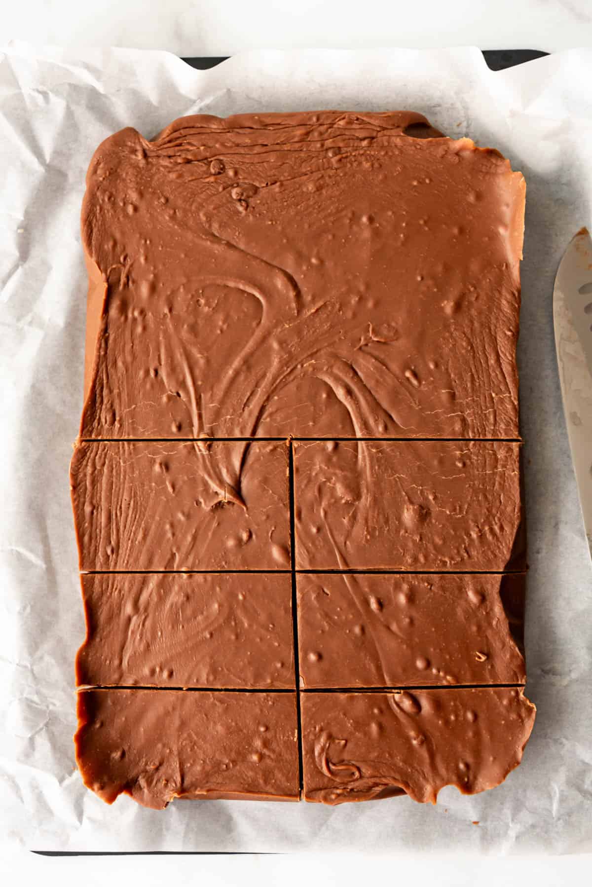 An image of a slab of chocolate fudge made with evaporated milk and marshmallows being cut into bricks.