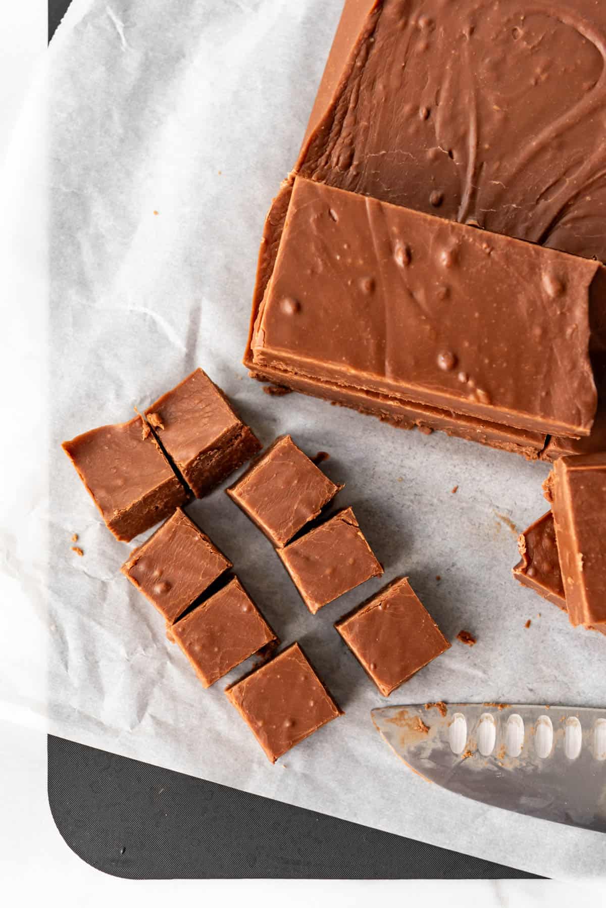 An image of creamy, smooth fudge being cut into squares for serving.