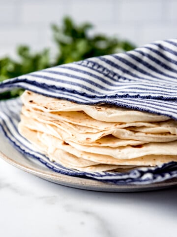An image of homemade flour tortillas wrapped in a towel to stay soft.