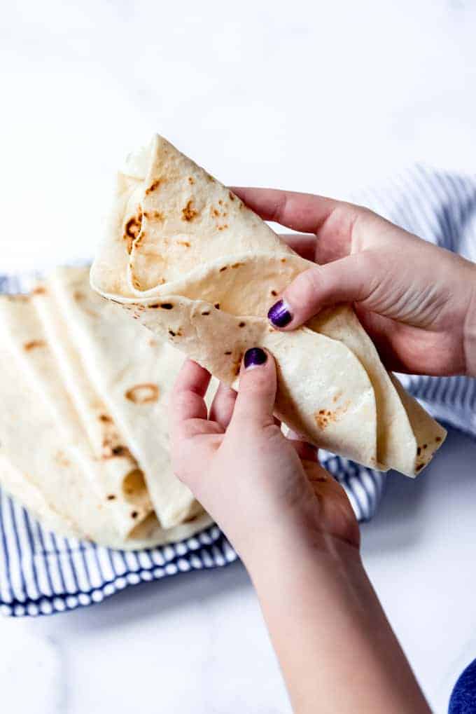 An image of hands holding a folded soft flour tortilla.