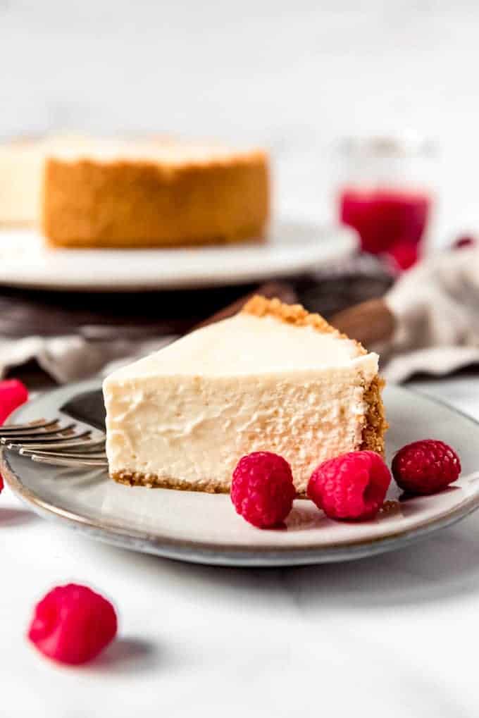 An image of a slice of creamy plain cheesecake with raspberries on the side.