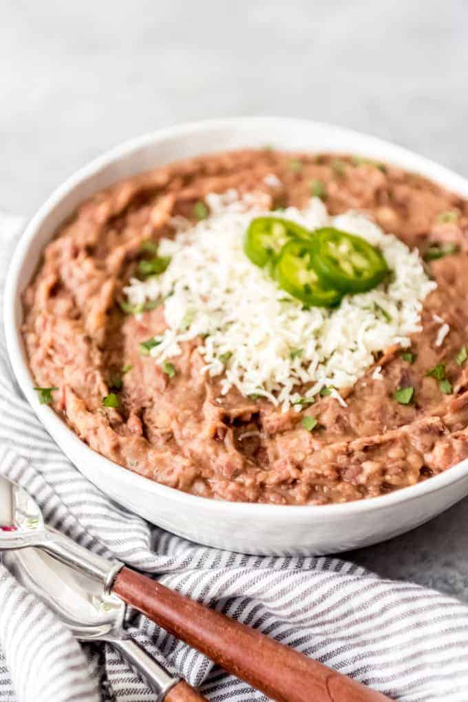 An image of a bowl of refried beans topped with shredded Monterey Jack cheese and sliced jalapenos.
