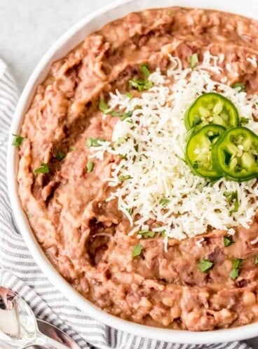 a white bowl of refried beans topped with cheese and sliced jalapenos