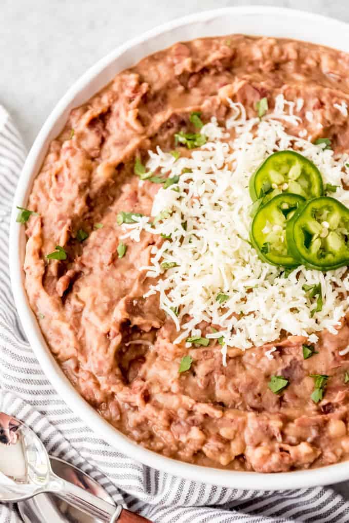 An image of a large bowl of instant pot refried beans with montery jack cheese and jalapenos on top.
